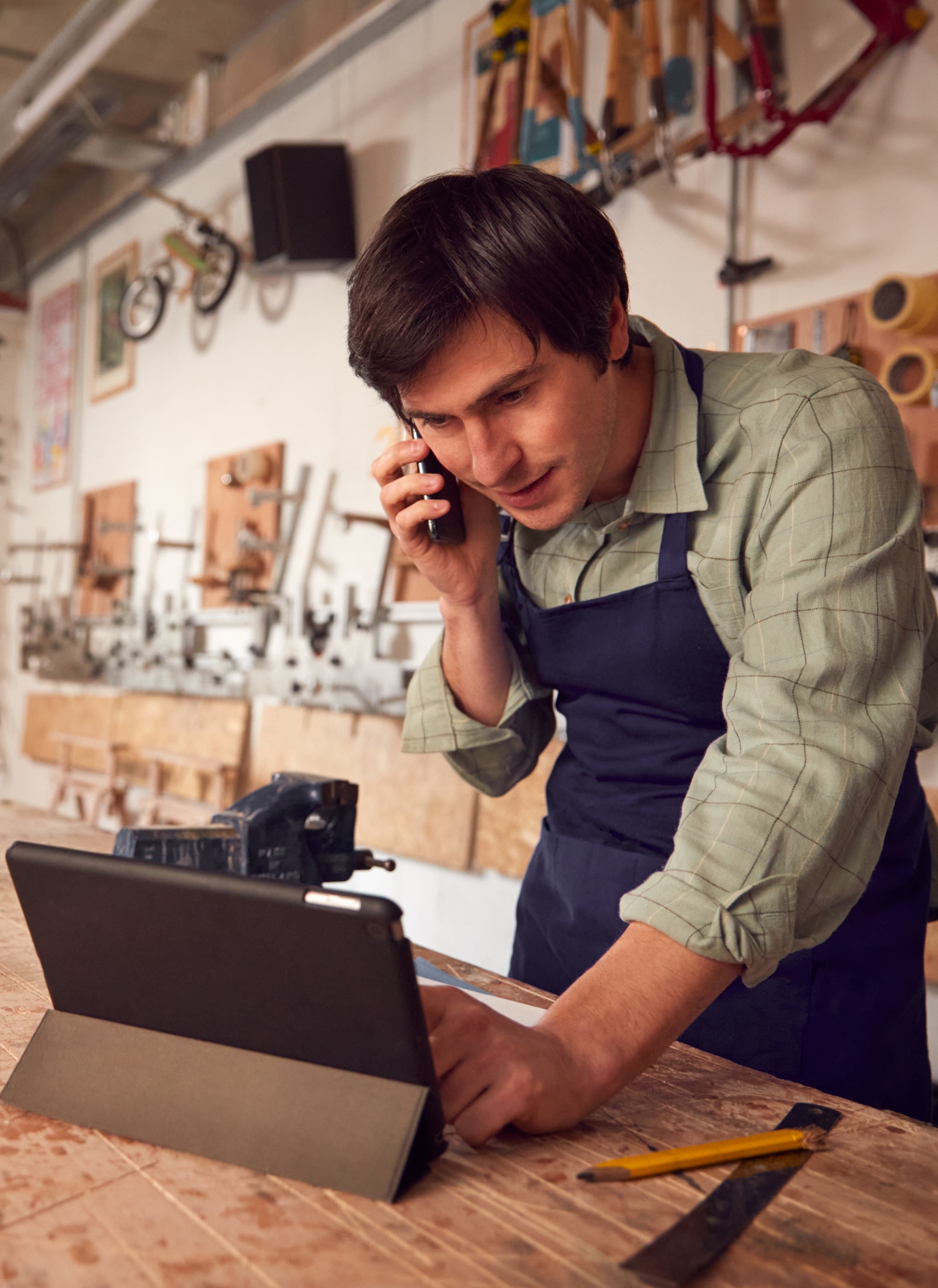 Male,Business,Owner,In,Workshop,Using,Digital,Tablet,And,Making Male Business Owner In Workshop Using Digital Tablet And Making Call On Mobile Phone